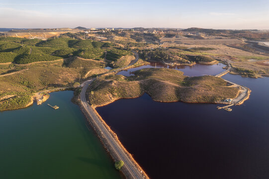 Aerial view of the winding road splitting waters of contrasting hues, where earthy reds meet deep blues and greens, Minas de Riotinto, Andalusia, Spain.