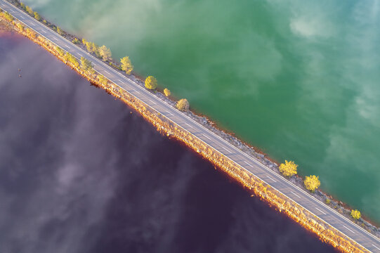 Aerial view of a road cutting through waters of contrasting colors, a stark divide between the green and purple, Minas de Riotinto, Andalusia, Spain.