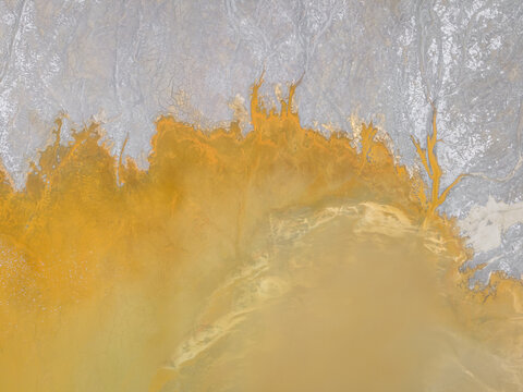 Aerial view of fiery ochre hues bleed into pale, cracked earth, creating an otherworldly landscape in stark contrast, Rio Tinto, Andalusia, Spain.