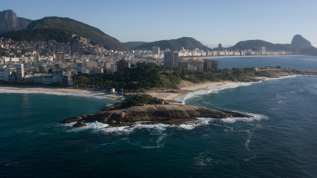 Aerial view of the rocky coastline meeting the city's edge, where waves crash against the shore near Arpoador, Rio de Janeiro, State of Rio de Janeiro, Brazil.