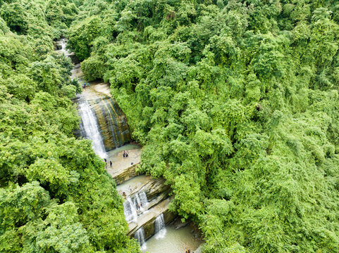Aerial view of the Khoiyachora waterfall cascading through a verdant jungle, its tiered descent a stark contrast to the surrounding dense canopy, Minsarai, Bangladesh.