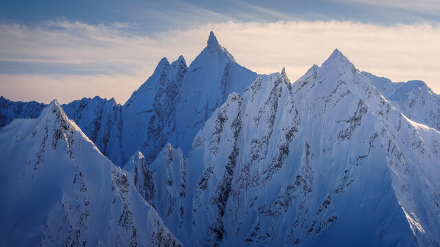 Aerial view of snow-capped peaks rise in jagged splendor, their icy ridges catching the soft light of the horizon, Valdez, Alaska, United States.