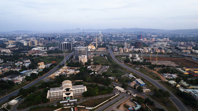 Aerial view of a sprawling cityscape reveals modern buildings and open roads under a hazy sky, with the National Mosque standing prominently, Abuja, Federal Capital Territory, Nigeria.