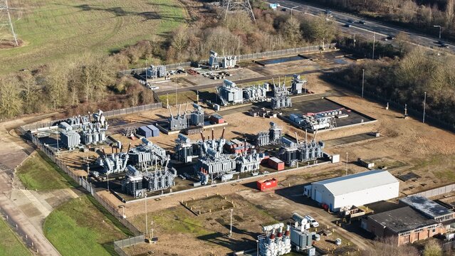 Aerial view of the National Grid Sundon Substation, a sprawling network of transformers and power lines against a backdrop of muted winter trees, Luton, United Kingdom.