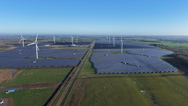 Aerial view of a vast checkerboard of solar panels and wind turbines under a crisp blue sky, a testament to renewable energy, Chelverston, United Kingdom.