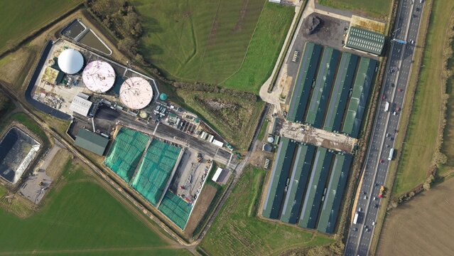 Aerial view of the Horse Close Green Power facility with its silver tanks, green netted areas, and long buildings adjacent to the motorway, Horse Close Green Power, Northampton, United Kingdom.