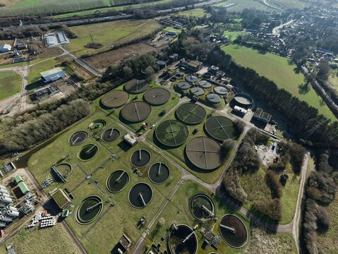 Aerial view of circular sewage tanks contrasting against the surrounding green fields and sparse winter trees, Luton, United Kingdom.