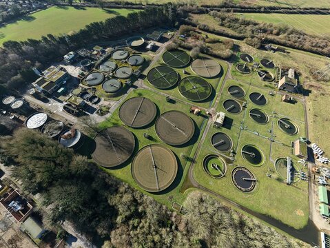 Aerial view of circular sewage tanks contrasting against the earthy tones of the surrounding landscape, where the industrial meets the natural, Luton, United Kingdom.