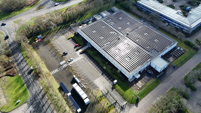 Aerial view of a modern building with solar panels gleaming under the sun, casting shadows on the parking lot, Milton Keynes, United Kingdom.