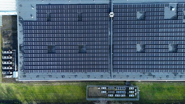Aerial view of rows of solar panels gleaming atop a building, contrasting against the surrounding green landscape, Milton Keynes, United Kingdom.