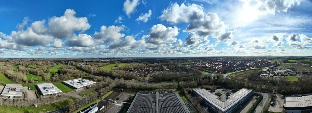 Aerial view of modern buildings and lush greenery under a bright, cloud-scattered sky in Milton Keynes, United Kingdom.