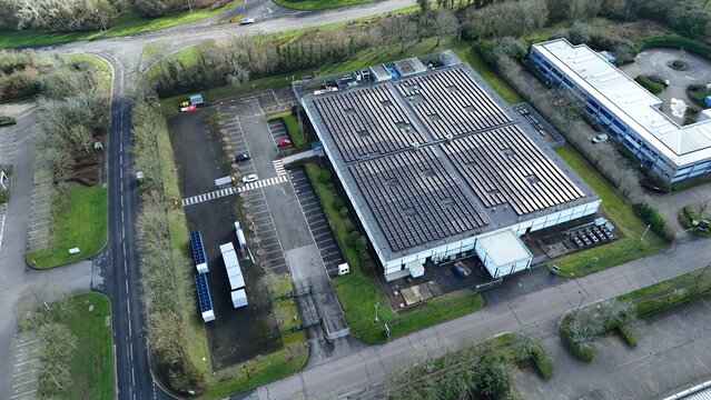 Aerial view of the nLighten Data Centre, a modern building with solar panels glinting under the diffused light, standing amidst green trees, Milton Keynes, United Kingdom.