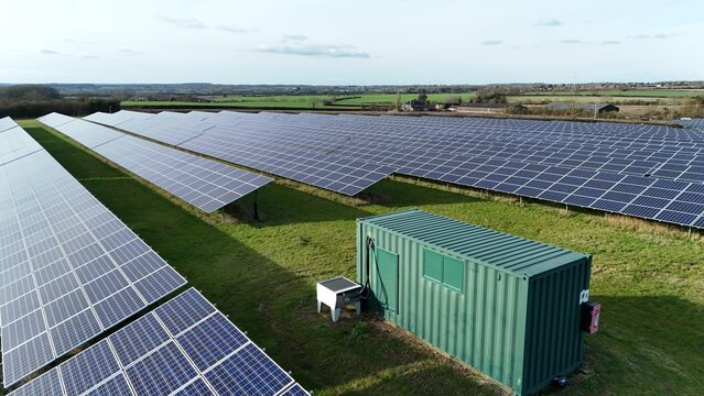 Aerial view of gleaming solar panels stretch across the verdant landscape, reflecting the sky's soft light, a testament to sustainable energy near Hartwell Solar Farm, Milton Keynes, United Kingdom.