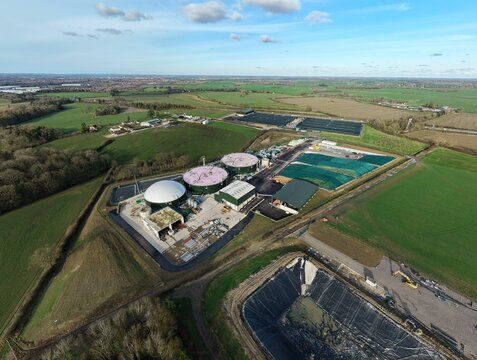 Aerial view of a biogas plant with its cylindrical structures and storage tanks surrounded by a patchwork of green fields, Horse Close Green Power, Northampton, United Kingdom.
