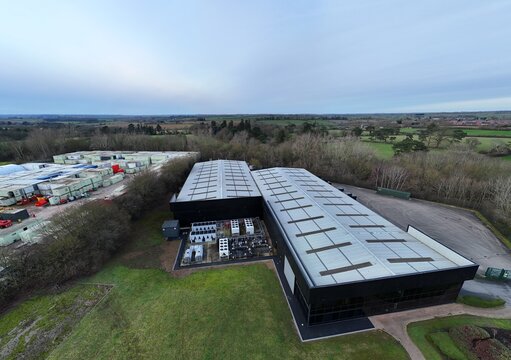 Aerial view of the modern Node4 Data Centre with its dark facade contrasting against the surrounding green fields and distant trees, Northampton, United Kingdom.