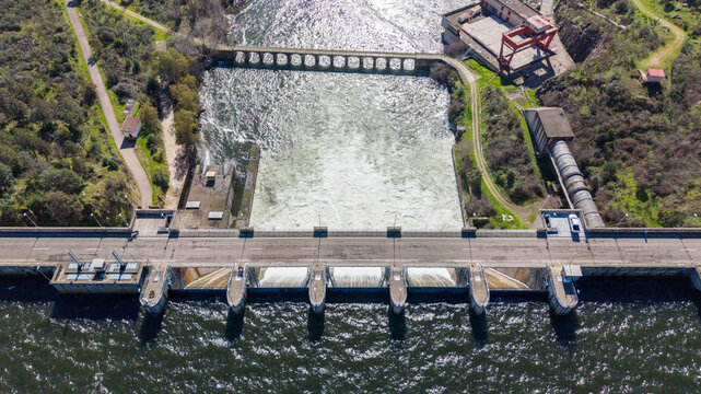 Aerial view of the dam structure cutting through the landscape, with the reservoir's waters creating a stark contrast against the concrete, Caceres, Caceres, Espana.