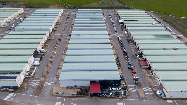 Aerial view of rows of buildings with gray roofs and parked vehicles, reflecting a structured industrial zone bathed in soft light, Caceres, Extremadura, Spain.