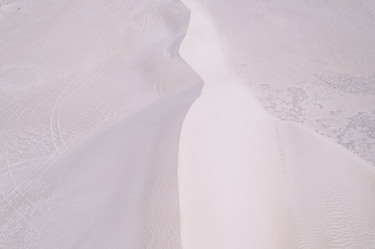 Aerial view of undulating white sand dunes, etched with delicate patterns of wind and time, rise in stark contrast against the pale horizon, Lancelin, Western Australia, Australia.