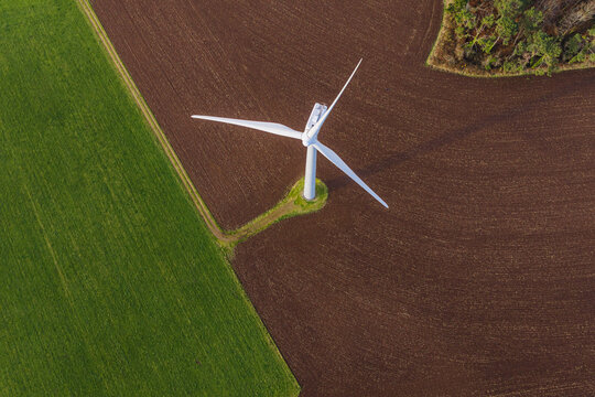Aerial view of a solitary wind turbine stands in stark contrast against the patchwork of vibrant green fields and rich brown soil, Plozevet, Brittany, France.