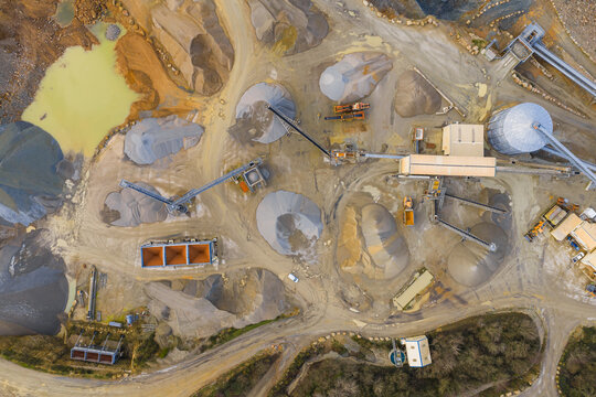 Aerial view of a quarry's geometric patterns of gravel piles and machinery, a stark contrast against the muddy pools, Gourlizon, Brittany, France.