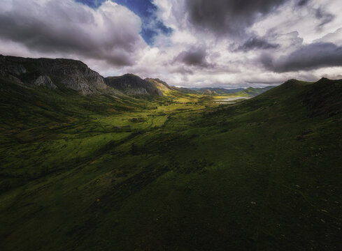 Aerial view of undulating green hills and rocky mountains under a dramatic sky, Aralla de Luna, Castilla y Leon, Spain.
