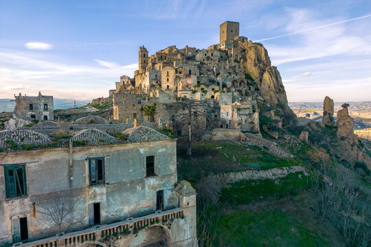 Aerial view of the abandoned medieval village clinging to a rocky outcrop, buildings weathered by time under a vast sky, Craco, Basilicata, Italy.