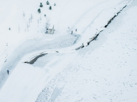 Aerial view of a snow-covered landscape bisected by a dark, winding road near a small structure, stark against the white expanse, Vilnius, Lithuania.