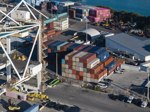 Miami, USA - 07 February 2026: Aerial view of a bustling port with stacks of multicolored containers casting shadows across the concrete, a vibrant mix of commerce and industry meeting the horizon.
