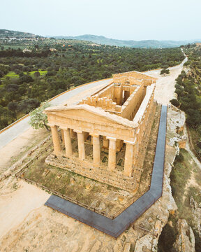 Aerial view of the ancient Temple of Concordia standing majestically against the backdrop of a lush valley, its weathered stones glowing warmly under the Sicilian sun, Agrigento, Sicily, Italy.