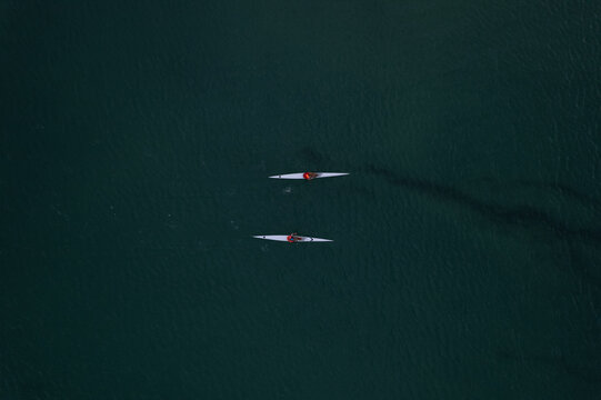 Aerial view of two kayakers glide through the dark waters of a river, leaving trails like ink on jade, Mandurah, Western Australia, Australia.