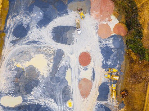 Aerial view of earthworks with multiple piles of colored earth, heavy machinery, and tracks creating abstract patterns, Plouasne, Brittany, France.
