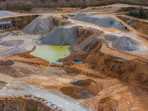 Aerial view of a quarry's harsh landscape where stone piles contrast with the unusual green pond, Gourlizon, Brittany, France.