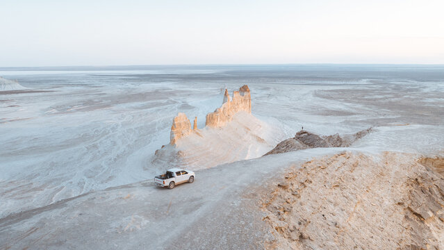 Aerial view of chalk mountains juxtapose with the vast, flat horizon, where a lone vehicle and distant figure accentuates the scale of the landscape, Aktau, Mangystau Region, Kazakhstan.