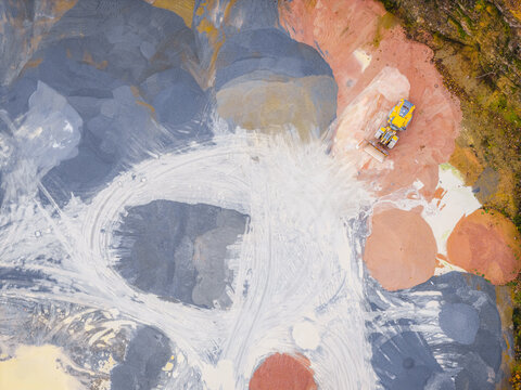 Aerial view of a lone yellow bulldozer carving paths through the vibrant, multi-hued quarry's landscape of Plouasne, Brittany, France.