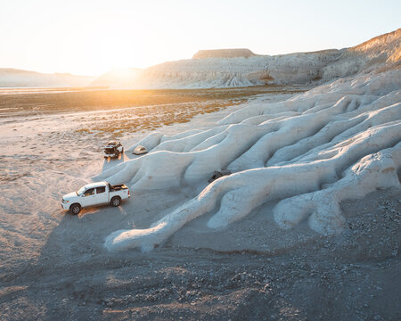 Aerial view of the sun kissing the chalky white ridges and rugged terrain where off-road vehicles navigate the stark landscape, Mangystau Region, Kazakhstan.