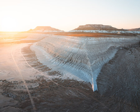 Aerial view of stark, sun-baked earth formations reveal nature's artistry in textured layers, contrasted by the soft, golden glow of the setting sun, , Mangystau, Mangystau Region, Kazakhstan.