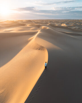 Aerial view of a solitary figure traversing the undulating dunes, bathed in the warm glow of the setting sun, Senek, Mangystau Region, Kazakhstan.