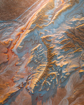 Aerial view of the sun-kissed earth unveils a tapestry of golden canyons and pale blue sediments, etched by time and elements, Kyzylkum, Mangystau Region, Kazakhstan.
