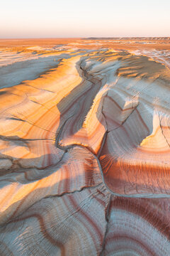 Aerial view of sun-kissed, undulating layers of earth reveal a tapestry of warm oranges and cool whites, etched by shadows, painting a surreal landscape, Kyzylkum, Mangystau Region, Kazakhstan.