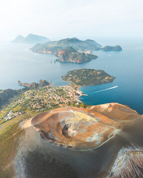 Aerial view of the dramatic volcanic landscape of Vulcano Island, its crater a palette of ochre and umber against the azure sea, Vulcano, Sicily, Italy.