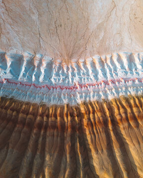 Aerial view of sun-baked earth, a canvas of ochre and beige, carved with intricate patterns and subtle textures creating a surreal landscape, Aktau, Mangystau Region, Kazakhstan.