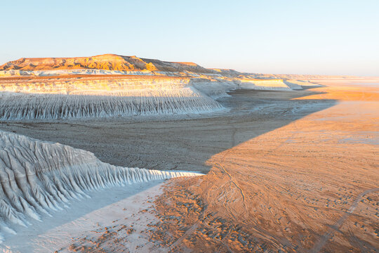 Aerial view of the stark, sun-kissed cliffs and vast, rippled plains create a mesmerizing contrast of light and shadow in the desolate landscape, Aktau, Mangystau Region, Kazakhstan.
