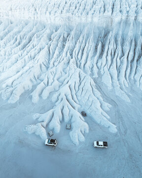 Aerial view of chalky canyons carved by time and weather, where two vehicles rest at the base of the formations, Mangystau Region, Kazakhstan.