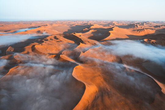 Aerial view of fog rolling through towering dunes, creating a surreal landscape of contrasting colors and textures, Sossusvlei, Hardap Region, Namibia.