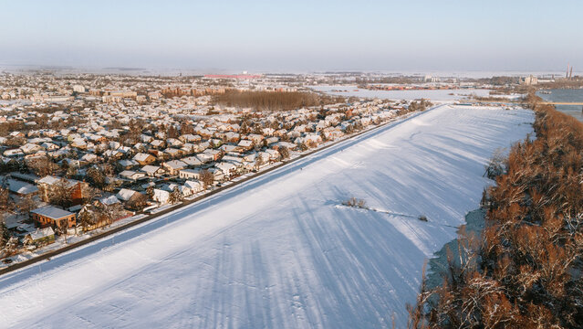 Aerial view of a snow-blanketed town meeting a frozen river under a pale winter sky, the landscape a study in whites and muted browns, Sremska Mitrovica, Vojvodina, Serbia.