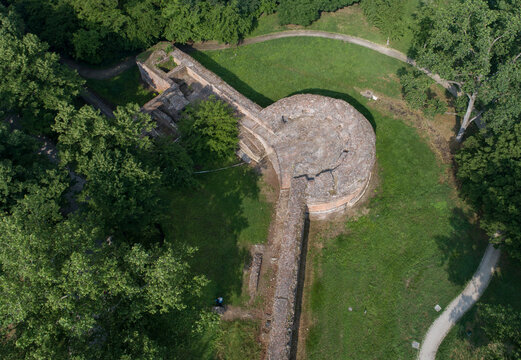 Aerial view of a stone fortress, surrounded by a dense forest, its ancient walls bathed in warm sunlight, Ferrara, Emilia-Romagna, Italy.