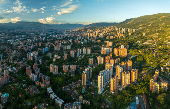 Aerial view of a dense urban sprawl where buildings rise amidst a sea of green, nestled beneath rolling hills, Medellin, Antioquia, Colombia.