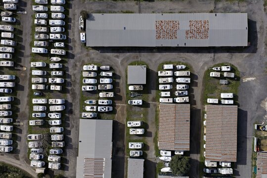 Aerial view of rows of parked recreational vehicles in a storage lot, reflecting the harsh sunlight, creating a geometric pattern of white roofs, Rome, Lazio, Italy.