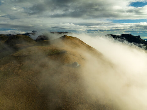 Aerial view of mist rolling over the hillsides, with a small building visible, creating a surreal landscape of soft textures and muted tones, Manizales, Caldas, Colombia.