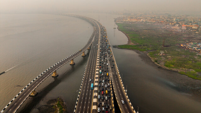 Aerial view of the Third Mainland Bridge cutting through the water, a ribbon of grey amidst the surrounding muted earth tones, Lagos, Lagos, Nigeria.
